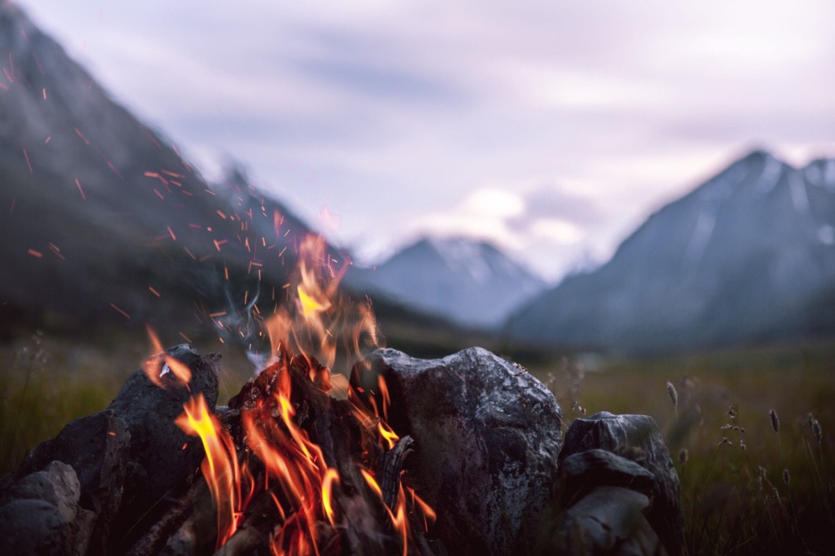 A campfire glowing at dusk with mountains in the background